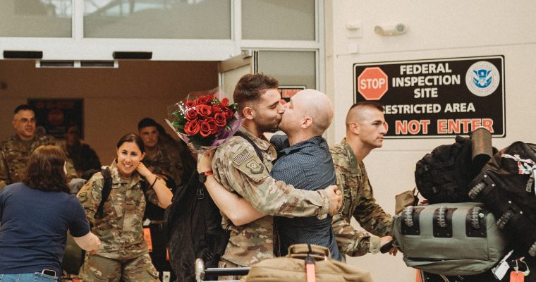 gay couple holding red roses kissing when service member comes home from deployment
