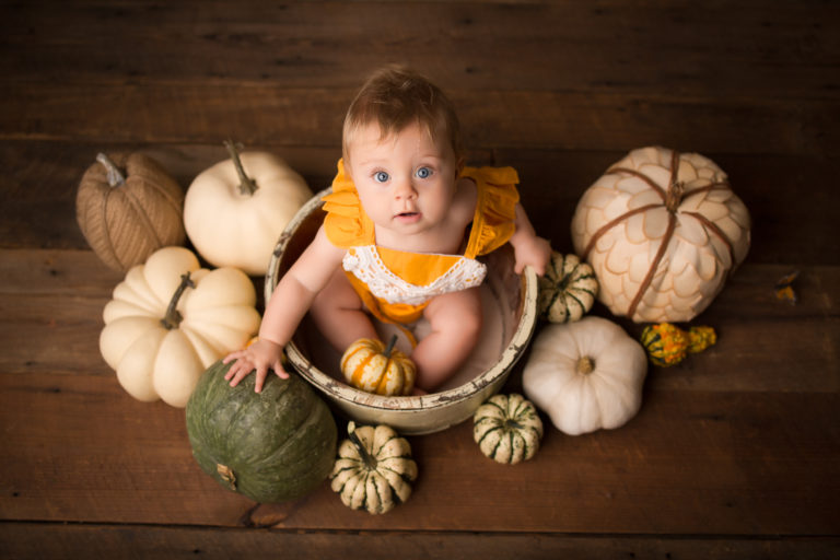 baby in wooden bowl surrounded by pumpkins