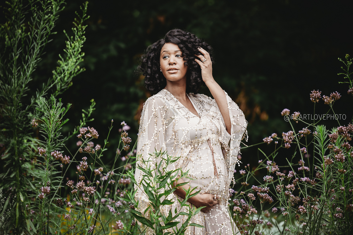 Black woman holding her pregnant belly in a gold gown surrounded by wildflowers