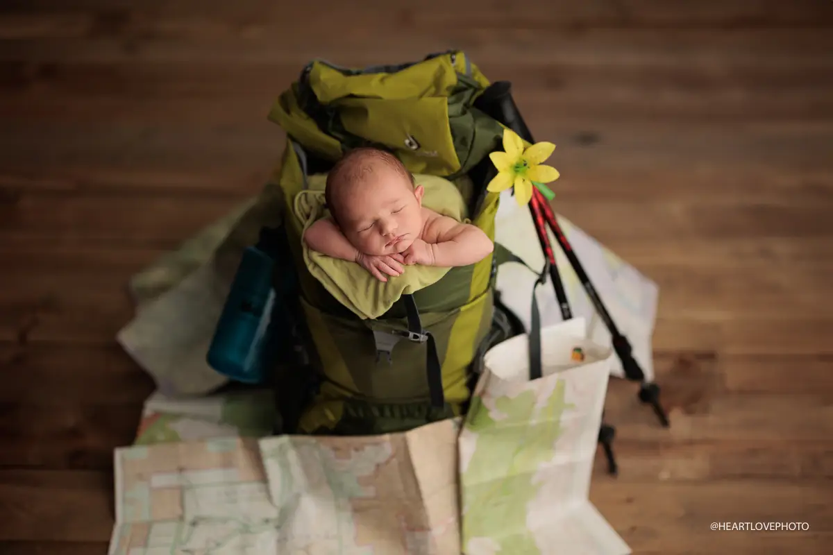Newborn baby posed in large camping backpack surrounded by trail maps