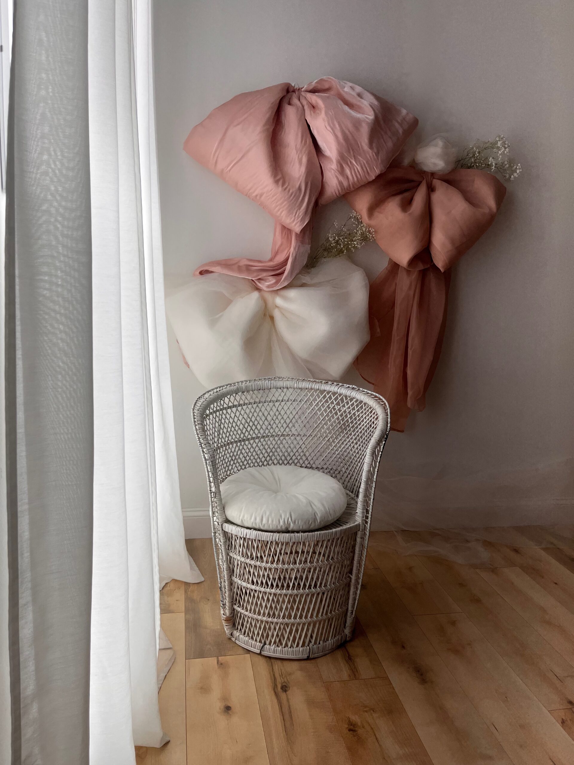 large blush pink and ivory bows made from silk and tulle with white rattan barrel chair next to a window